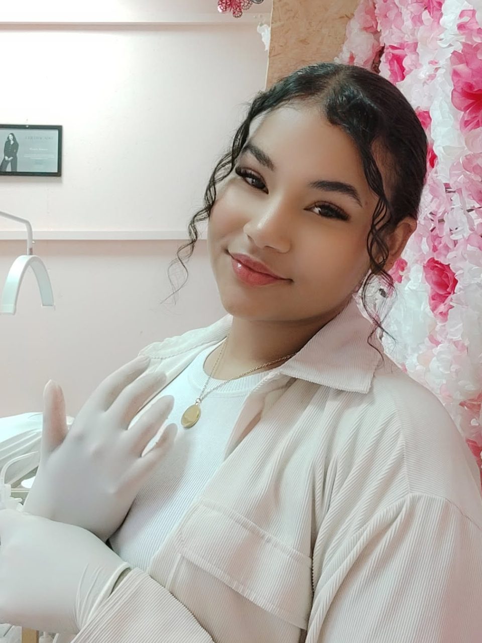 Aby, del equipo de Bloom, con la bata y los guantes puestos en la cabina de faciales, junto a la pared de flores rosas