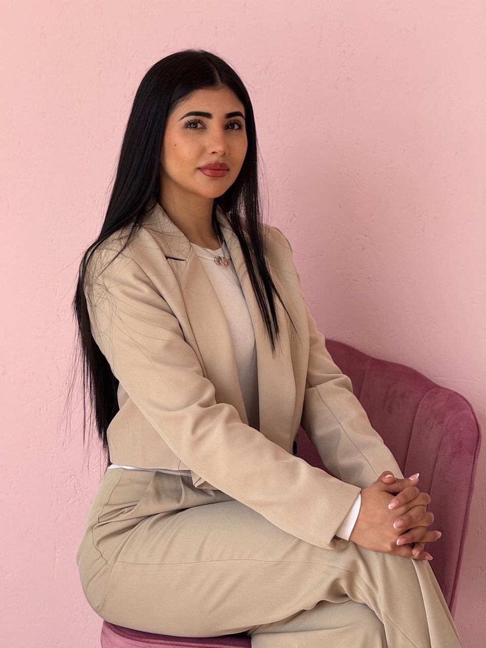 Verónica Gamarra, titular de Bloom, sentada en un sillón de terciopelo burdeos y con traje beige, delante de la pared rosa del centro
