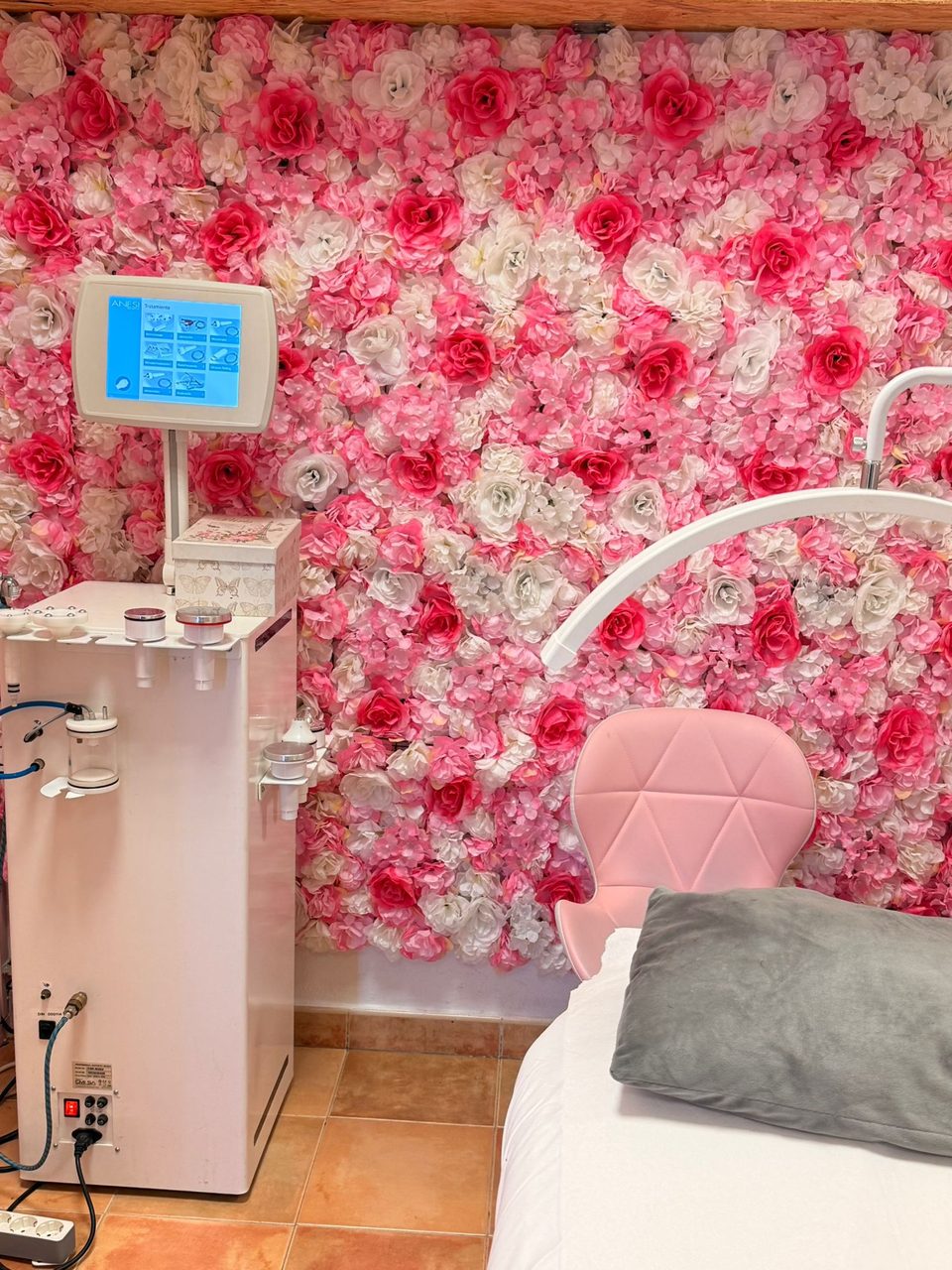 Cabina de faciales de Bloom: la pared cubierta de flores rosas y blancas, el aparato de tratamiento, el sillón rosa y la camilla